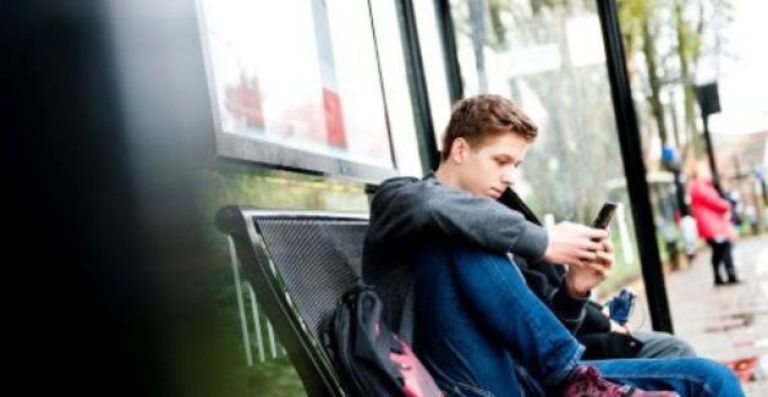 Jongen bij de bushalte leest boek op zijn smartphone